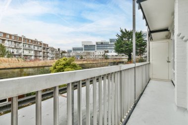 Arka planda bazı binaların olduğu bir balkon ve bir apartman penceresinden görüldüğü gibi içinden akan bir nehir.