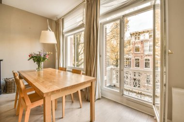 büyük bir pencerenin önünde bir masa ve sandalyeler. Dışarıdaki verandaya açılan açık bir kapı.