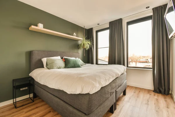 a bedroom with green walls and wood flooring in the room, there is a bed that has pillows on it