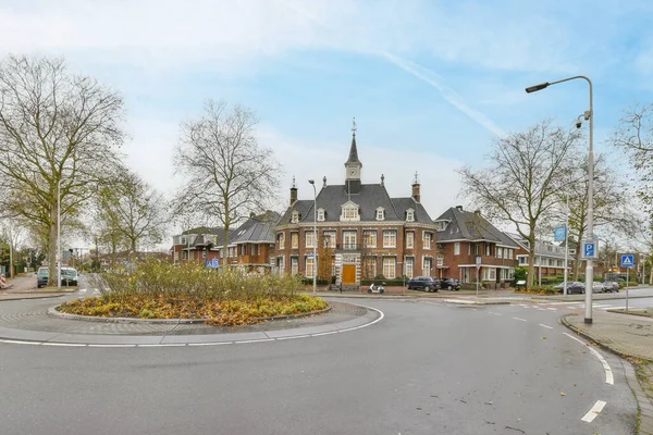 stock image Amsterdam, Netherlands - 10 April, 2021: a street corner with a church in the middle and trees on both sides, some cars parked at the other side