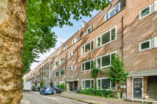 Amsterdam, Hollanda - 10 Nisan 2021: Caddenin her iki tarafındaki tuğla bina ve ağaçların önüne park edilmiş bir cadde bir apartman binasıdır.