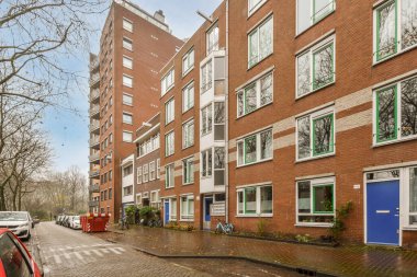 Amsterdam, Hollanda - 10 Nisan 2021: Kenarında arabalar, arka tarafında binalar olan bir şehir caddesi, hepsi pencerelerine tuğla örülmüş.