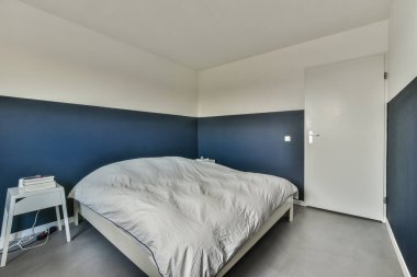 Yatak başlığının etrafında mavi duvarlar ve beyaz süslemeler olan, koyu maviye boyanmış bir oda.