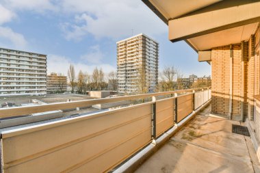Arka planda bazı binalar ve üzerinde mavi gökyüzü olan bir balkon güneşli bir günde bir apartmandan görüldüğü gibi.