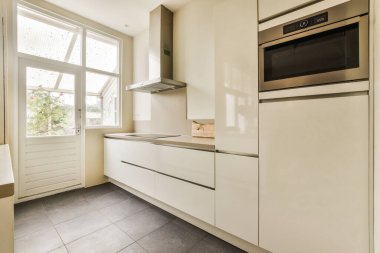 Açık bir pencerenin önünde beyaz dolapları ve siyah fayansları olan bir mutfak.