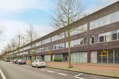 Amsterdam, Hollanda - 10 Nisan 2021: Kenarında arabalar ve sokağın ortasında binalar olan bir şehir caddesi, hepsi tuğladan örülmüş.