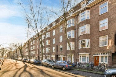 Amsterdam, Hollanda - 10 Nisan 2021: Pencereleri ve kapıları olan tuğladan apartmanların önüne park edilmiş bazı arabalar