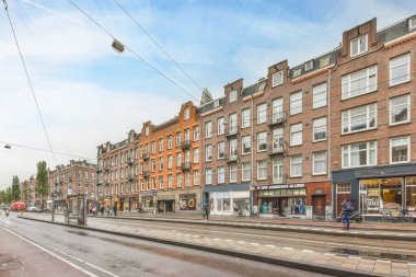 Amsterdam, Hollanda - 10 Nisan 2021: Her iki tarafında binalar olan bir şehir caddesi ve fotoğrafın ortasında yürüyen insanlar