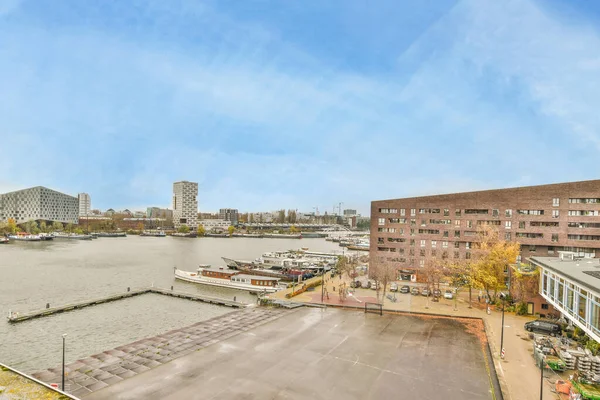 Amsterdam, Hollanda - 10 Nisan 2021: Bir binanın tepesinden nehrin aşağısına bakan bir şehir suda tekneleri ve diğer tarafta binaları olan bir şehir