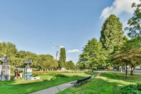 stock image Amsterdam, Netherlands - 10 April, 2021: a park with a bench in the middle and some trees on the other side of the park, there is a blue sky above