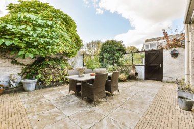 Beyaz boyanmış tuğla bir duvarın önünde, üzerinde sandalyeler, masa ve çömlekler olan bir teras.