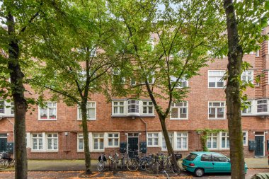 Ağaç ve yapraklarla yan yana duran bir apartmanın önüne parketmiş bisikletler.
