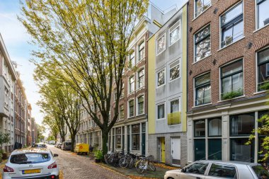 Amsterdam, Hollanda - 10 Nisan 2021: Bir apartmanın önündeki caddenin kenarına park edilmiş bazı arabalar, kaldırımda ağaçlar var.