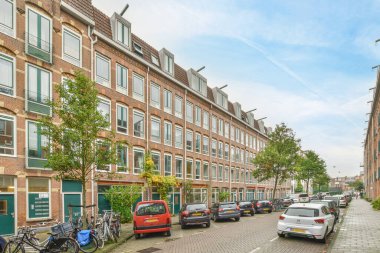 Amsterdam, Hollanda - 10 Nisan 2021: Bazı arabalar yeşil pencereli tuğla binaların önüne park etmiş.