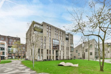 Amsterdam, Hollanda - 10 Nisan 2021: Binanın her iki tarafında yeşil çimenler ve çıplak ağaçlar olan bir şehrin ortasında bir apartman kompleksi