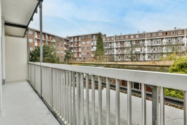 Arka planda bazı binalar ve şehrin sağ tarafında mavi gökyüzü olan bir balkon.