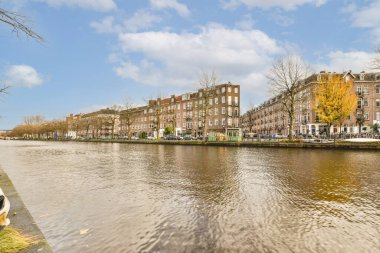 Güneşli bir günde, arka planda binalar ve ağaçlar olan bir nehir, su kenarından görüldüğü gibi.