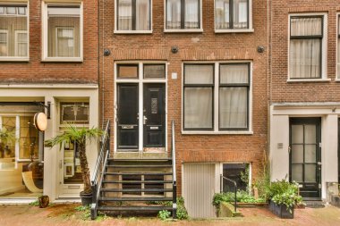 Önünde birkaç fabrika olan tuğla bir bina ve ikinci kata çıkan bir apartman kompleksi.