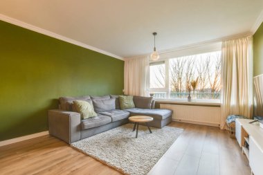 Duvarları yeşil, duvarları ahşap kaplı bir oturma odası. Köşesinde gri bir kanepe var.