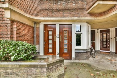 Ön kapıda bisikleti olan tuğladan bir ev ve binanın yanında büyüyen bitkiler.