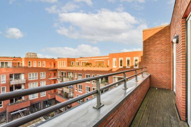 Kırmızı tuğlalı binalar ve arka planda mavi gökyüzü olan bir balkon bir apartmanın çatısından alındı.