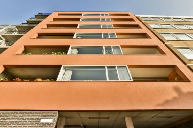 Balkon penceresinde bitkiler büyüyen bir apartman ve önünde mavi gökyüzü.