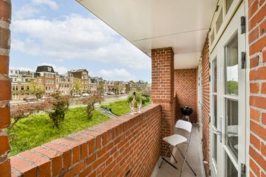 Kırmızı tuğlalı duvarlar ve pencereleri beyaz süslemeli bir balkon, uzaktaki bir şehir caddesine bakıyor.