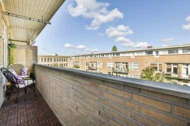 Amsterdam, Hollanda - 10 Nisan 2021: Bir sıra apartmanın önünde, tuğla duvarın kenarında sandalyeler ve masalar olan bir dış alan