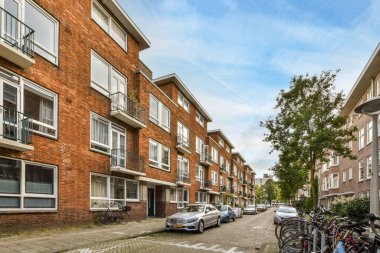 Amsterdam, Hollanda - 10 Nisan 2021: Tuğlalı binalar ve oy alanlarıyla dolu bir kentsel alanda bir caddenin kenarına parketmiş bisikletler