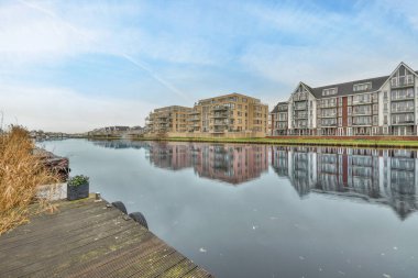 Amsterdam, Hollanda - 10 Nisan 2021: Arkaplanda binalar ve üzerinde mavi gökyüzü olan bir su kütlesi, nehrin karşısından görüldüğü gibi.