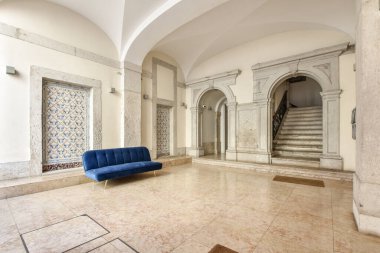 Ortasında mavi bir kanepe olan bir oturma odası ve diğer taraftaki başka bir odaya açılan kemerli bir kapı.