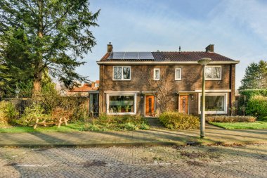 Amsterdam, Hollanda - 10 Nisan 2021: Tavanında güneş panelleri ve önünde iki pencere olan eski bir tuğla ev bir bahçe.