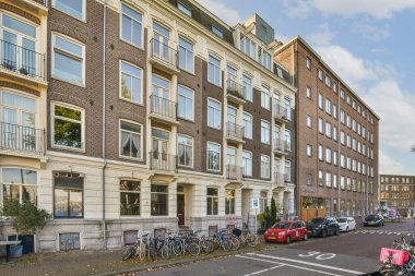 Amsterdam, Hollanda - 10 Nisan 2021: Birçok pencere ve balya bulunan bir apartmanın önündeki yolun kenarına parketmiş bisikletler