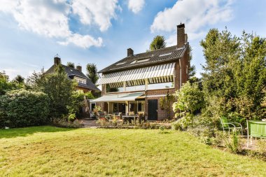 Evin her iki tarafında yeşil çimenler ve ağaçlar olan bir alanın ortasında bir ev.