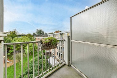 Amsterdam, Hollanda - 10 Nisan 2021: Korkuluklarda bitkiler ve arka planda mavi gökyüzü olan bir balkon, bir apartmanın balkon penceresinden alındı.