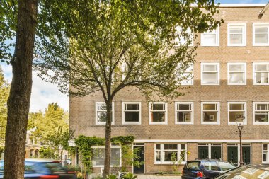 Önünde arabalar olan bir apartman ve yol kenarında ağaçlar olan bir apartman.