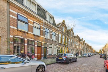 Bazı arabalar caddenin kenarına park etmiş. Pencereleri ve kapıları olan tuğlalı binaların önünde.