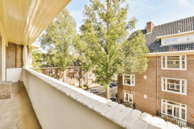 a balcony with trees and houses in the background on a sunny day, taken from an apartment window looking out onto the street