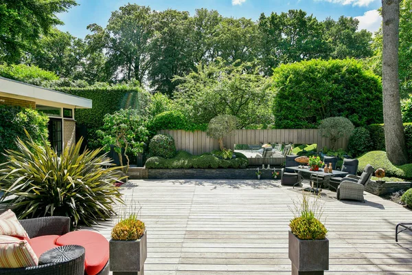 Amsterdam, Hollanda - 10 Nisan 2021: güneşli bir günde yemyeşil yapraklarla çevrili arka bahçesinde bahçe mobilyası ve ağaçları olan bir açık hava yaşam alanı