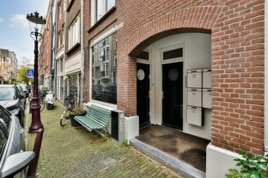 Önünde yeşil bir bank ve yanında beyaz bir araba olan tuğla bir bina.