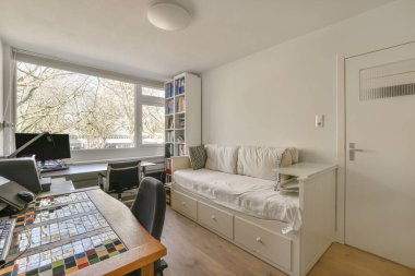 Pencerenin önündeki masada penceresi, masası ve bilgisayar monitörü olan bir oturma odası. Dışarıdaki ağaçlara bakıyor.