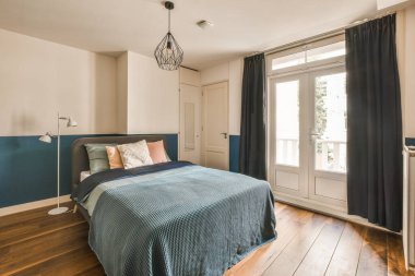 Odanın zemininde ahşap döşeme ve mavi yatak odası var. Balkona açılan açık bir kapı var.