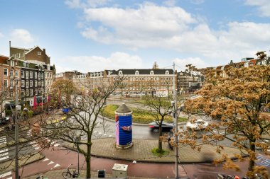 Amsterdam, Hollanda - 10 Nisan 2021: Önünde binalar ve ağaçlar olan bir şehir caddesi - güneşli bir günde bir gözlem noktasından çekildi.