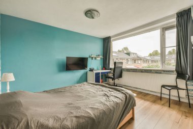 Yatağı, masası ve televizyonu olan bir yatak odası. Köşedeki penceresinde sokağa bakıyor.