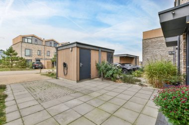 Amsterdam, Hollanda - 10 Nisan 2021: İki binanın önünde bazı bitki ve çiçeklerin bulunduğu bir dış alan, birinin yanına park edilmiş bir araba var.