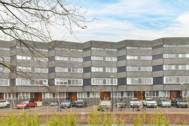 Amsterdam, Hollanda - 10 Nisan 2021: Otoparkın yanına park edilmiş bir apartman ve sokağın iki tarafında da ağaçlar var.