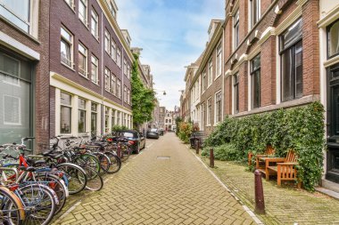 Amsterdam, Hollanda - 10 Nisan 2021: Tuğlalı bir caddenin kenarına park edilmiş bazı motosikletler, kentsel alanda büyüyen binalar ve bitkiler