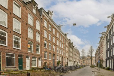 Kaldırımlara parketmiş bisikletli bir şehir caddesi ve binaların önünde yürüyen insanlar.,
