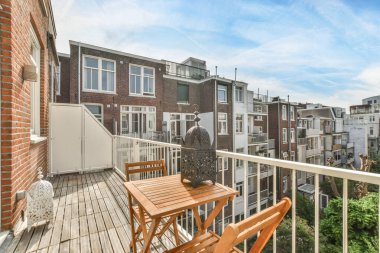 Amsterdam, Hollanda - 10 Nisan 2021: Ahşap sandalyeli ve masalı bir balkon, Londra 'da bir apartmandan sokağa bakıyor.