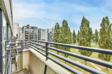 Amsterdam, Hollanda - 10 Nisan 2021: Arka planda ağaçlar ve binalar olan bir balkon, bir apartmanın içinden sokağa bakıyor.